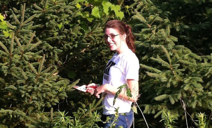 Hallie smiling holding shears in a grove of pine trees and mustang grape