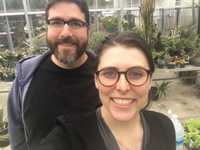 A man and a woman smiling at the camera while standing in a greenhouse